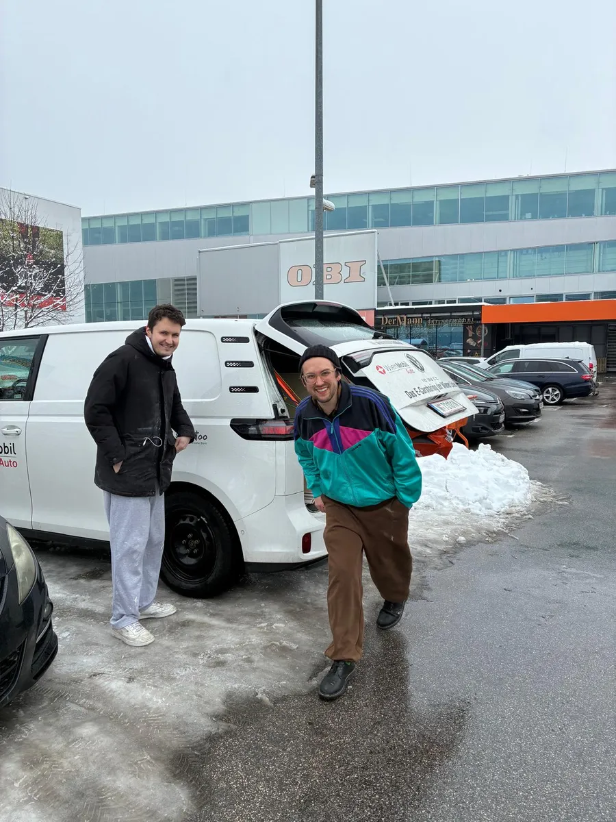 Zwei aus dem Team lachend vor dem vollgeladenen Transporter auf dem Baumarktparkplatz im Schnee
